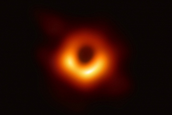 Неделю назад стало известно, что астрономы проекта Event Horizon Telescope (EHT) готовятся опубликовать первую в мире фотографию чёрной дыры. Сегодня это фото стало достоянием общественности. Ниже вы можете видеть этот самый снимок. Да, он не впечатляет. По крайней мере для тех, кто далёк от астрономии. Если же говорить о сложности получения такой фотографии, это действительно прорыв. Вопреки предположениям, на фото чёрная дыра не из центра нашей галактики. Астрономы сделали снимок сверхмассивной чёрной дыры, расположенной в центре эллиптической галактики Messier 87 (M 87), расположенной на расстоянии около 54 млн световых лет от нас. Фото самой галактики вы можете видеть ниже. Чёрная дыра в центре этой галактики, согласно расчётам, имеет массу в 6,5 млрд масс Солнца. Что касается размеров, тот самый горизонт событий, который и видно на снимке, имеет диаметр «всего» около 40 млрд км. Напомним, проект Event Horizon Telescope (EHT), благодаря которому и удалось сделать этот уже исторический снимок, представляет собой «объединение» множества телескопов по всей земле, что позволяет создать «виртуальный» телескоп «размером с Землю». Принцип работы такого массива радиотелескопов (все телескопы проекта относятся именно к этому типу) можно посмотреть на видео ниже. Что интересно, фактические наблюдения, результат которых мы видим на фото, проводились ещё в 2017 году, причём лишь на протяжении одной недели. Однако в итоге получилось несколько петабайт данных, обработка которых заняла многие месяцы. Вскоре к проекту EHT присоединятся ещё два телескопа (сейчас их восемь), так что возможности учёных расширятся ещё сильнее.